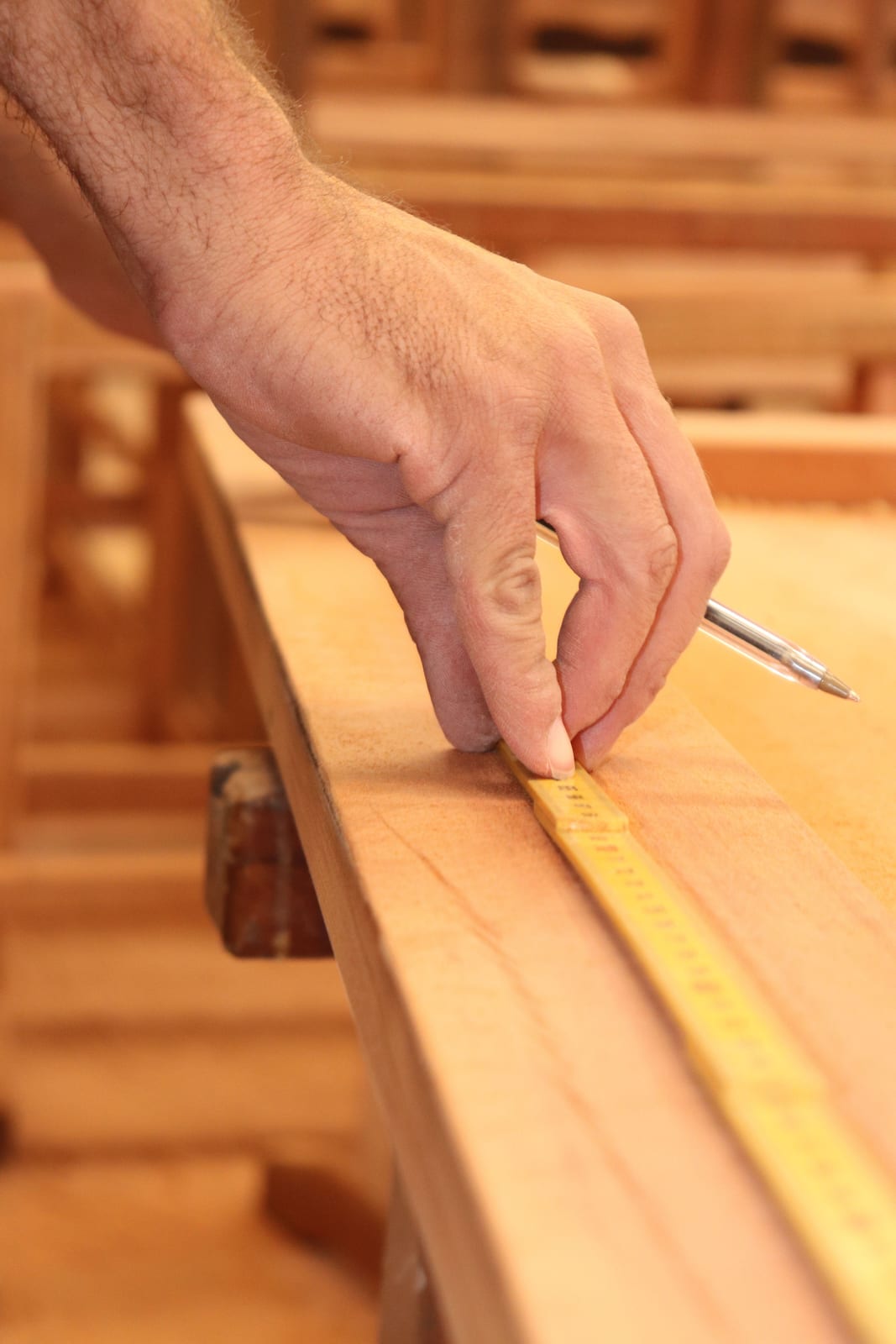 Schreiner vermisst einen Holzbalken mit Zollstock und Bleistift in der Werkstatt